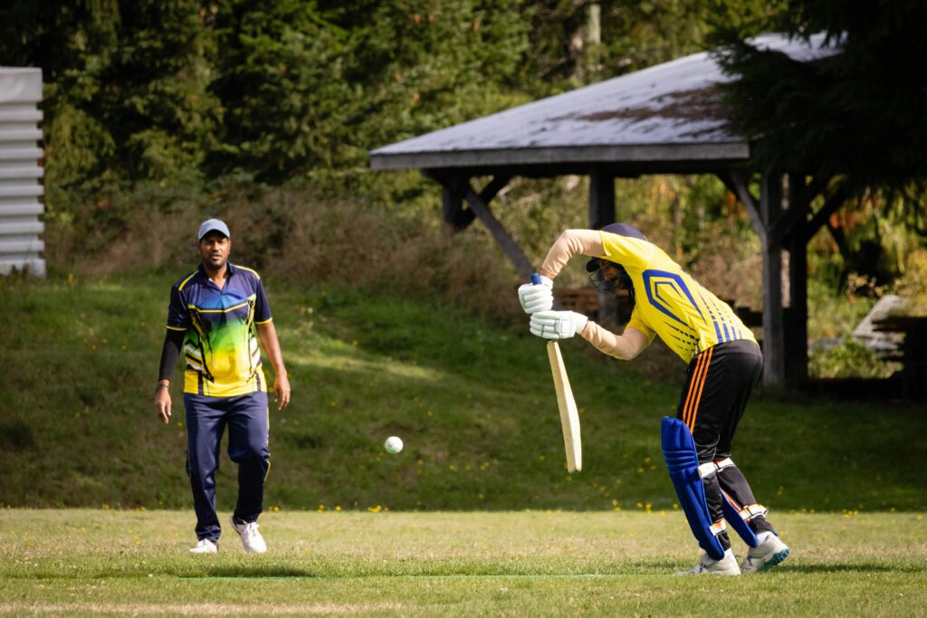 Two cricketers engaged in an outdoor match, focusing on batting and fielding tactics.