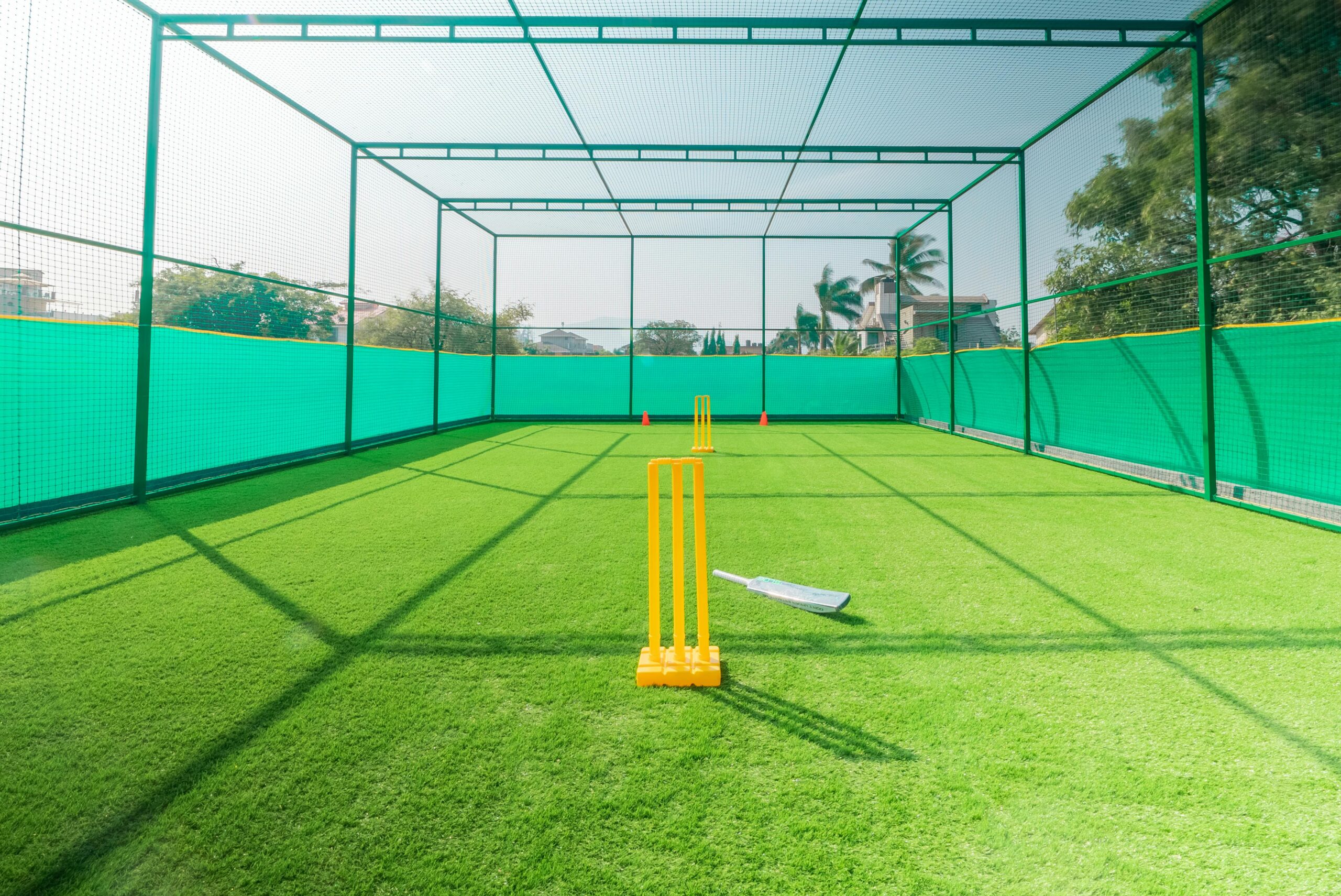 A cricket practice net with bright yellow stumps on a sunny day, ideal for training.